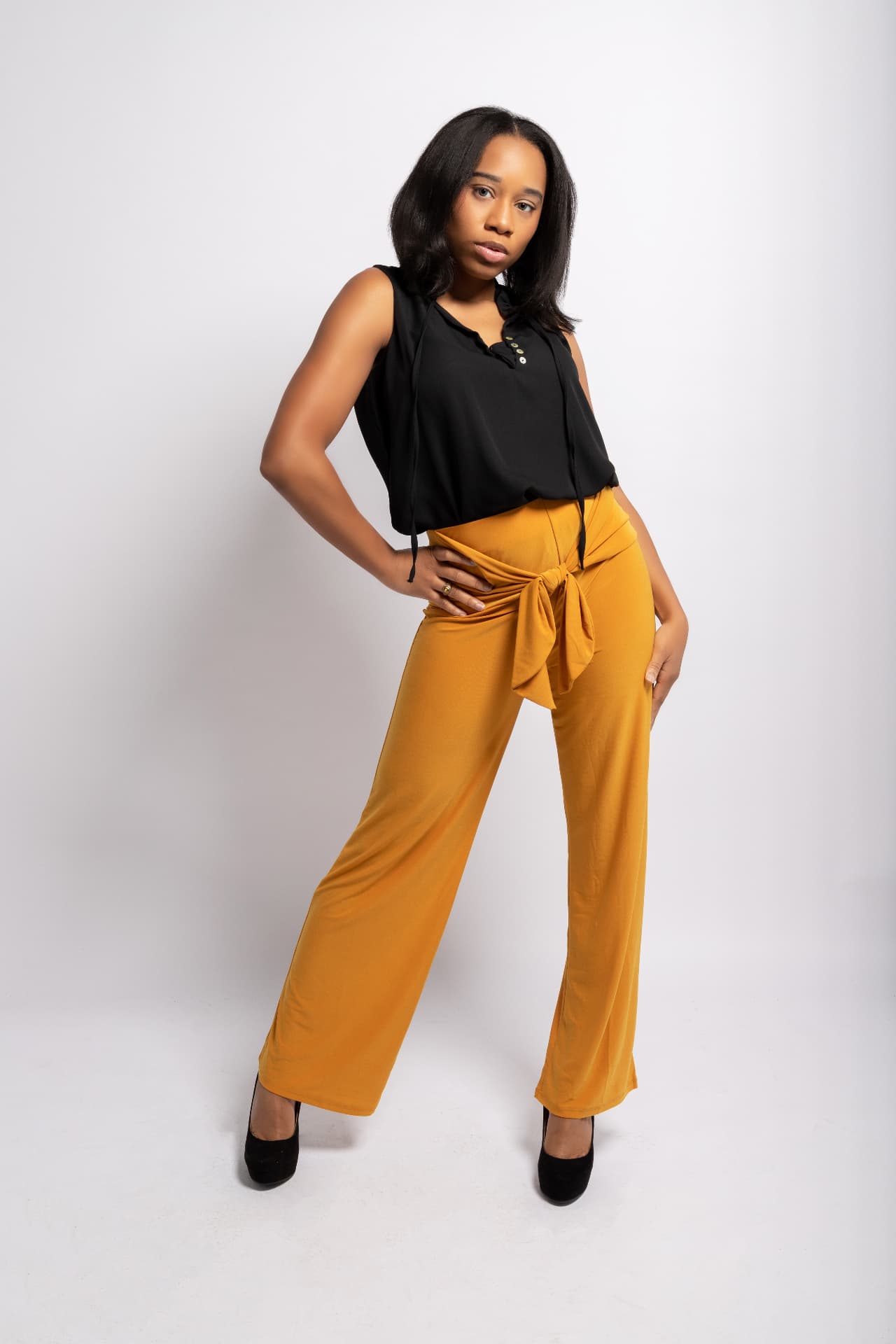 Taniya Patrick in a black top and mustard wide-leg trousers, full-length studio editorial portrait